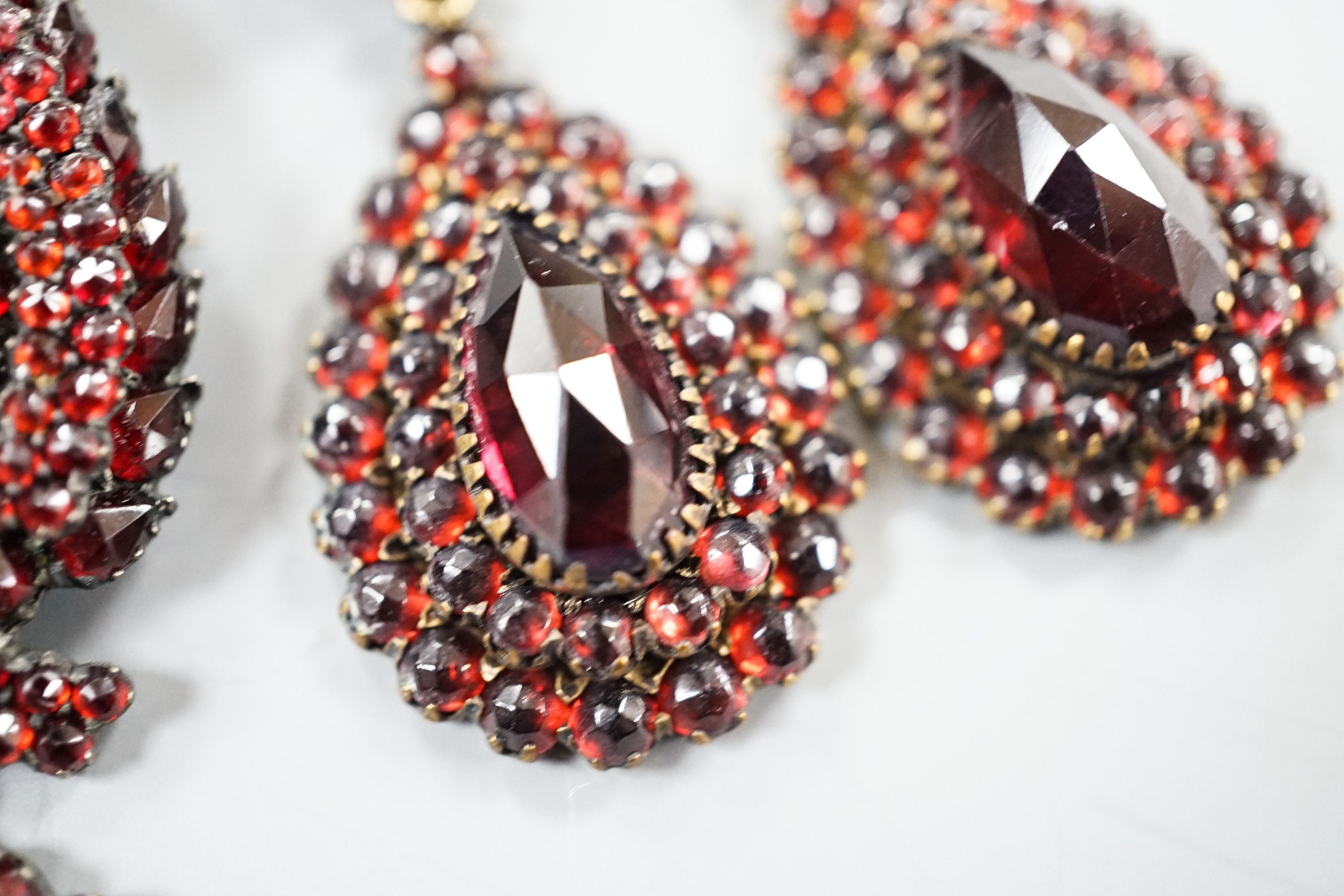 A pair of Victorian gilt metal and facet cut garnet set drop earrings, 51mm and a similar white metal and garnet set pendant brooch.